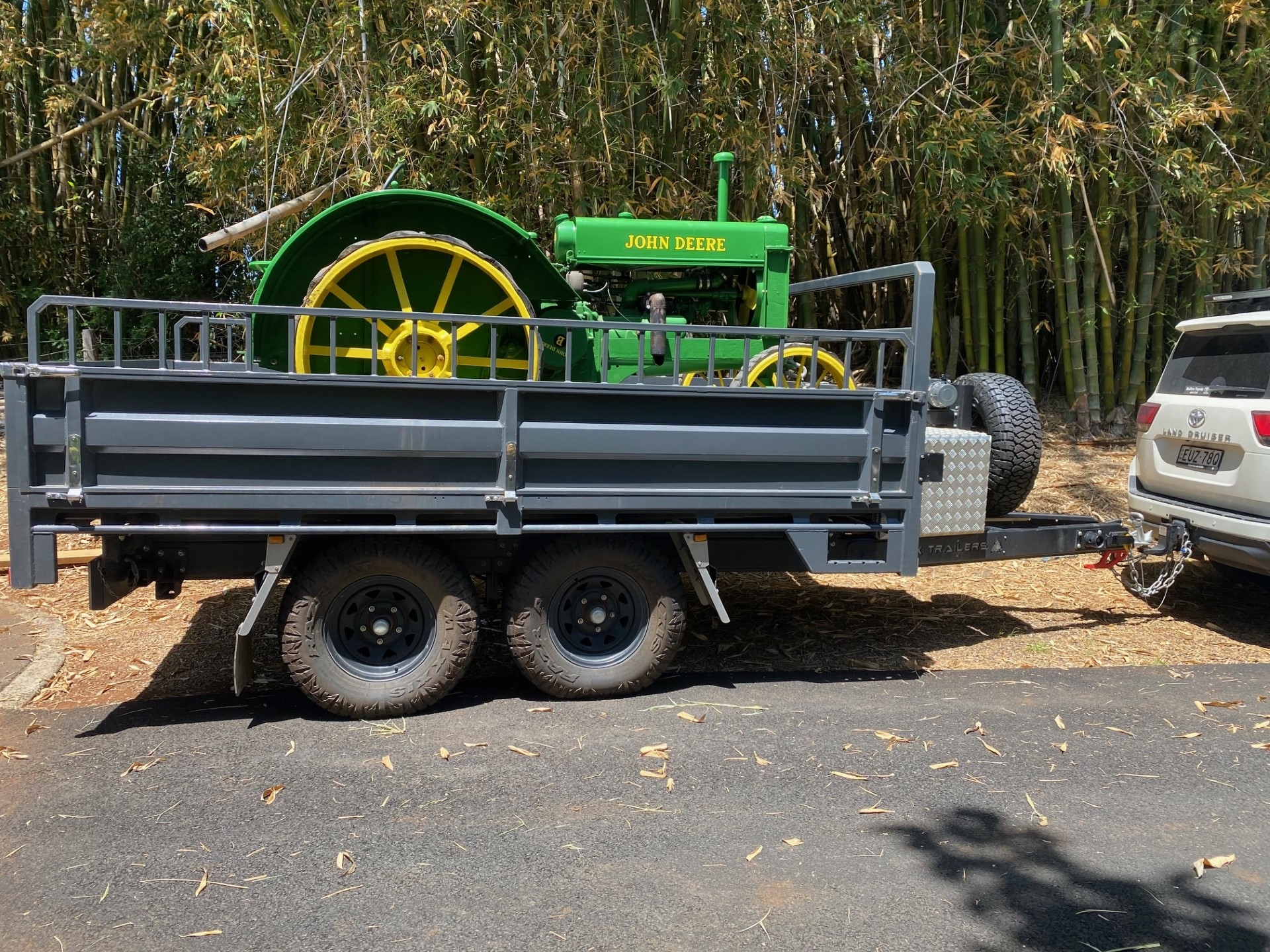 A Rear Tipper Trailer with vintage John Deere tractor on tray being towed behind Toyota Landcruiser. The trailer has hi-volume extender Dropsides and tandem axles with Maxxis Razr All Terrain Tyres.