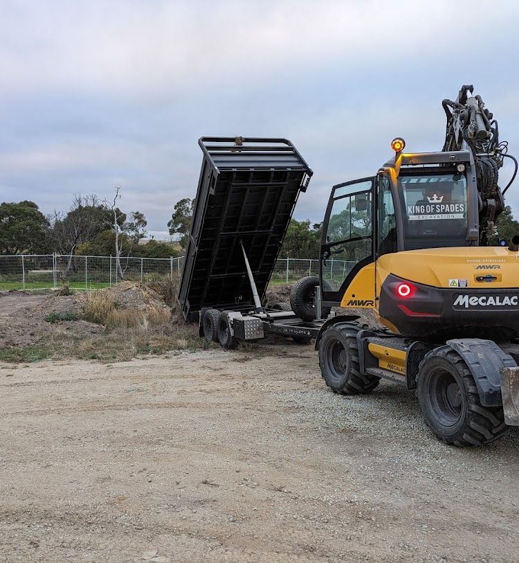 The King of Spades Excavation tipper at full tip, dropping a load of dirt while being towed by a mecalac excavator.