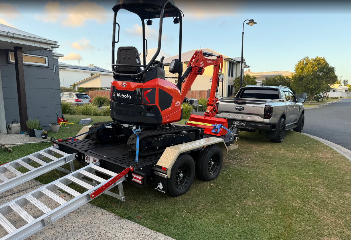 heavy duty custom flat top trailer for gee building at rural construction site with toolbox and canopy doors open.
