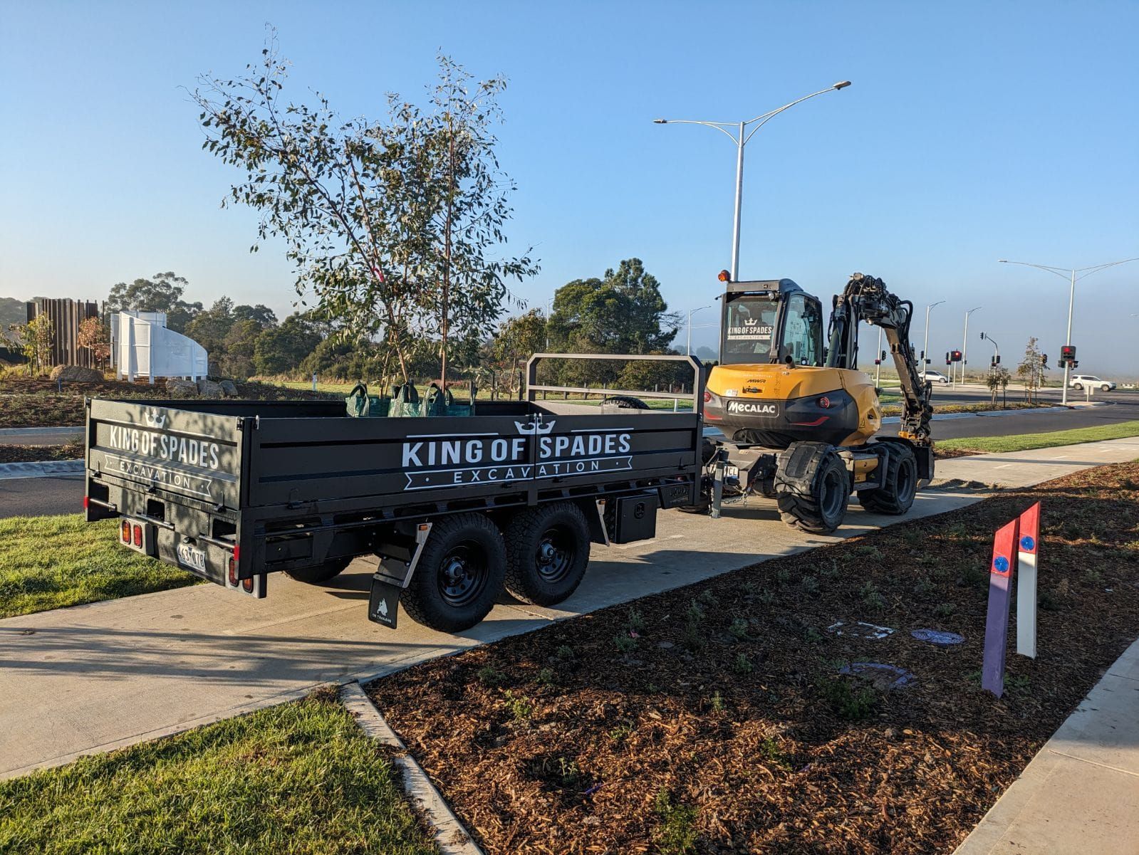 A tipper trailer at a commercial landscaping project. Being towed behind a large excavator.