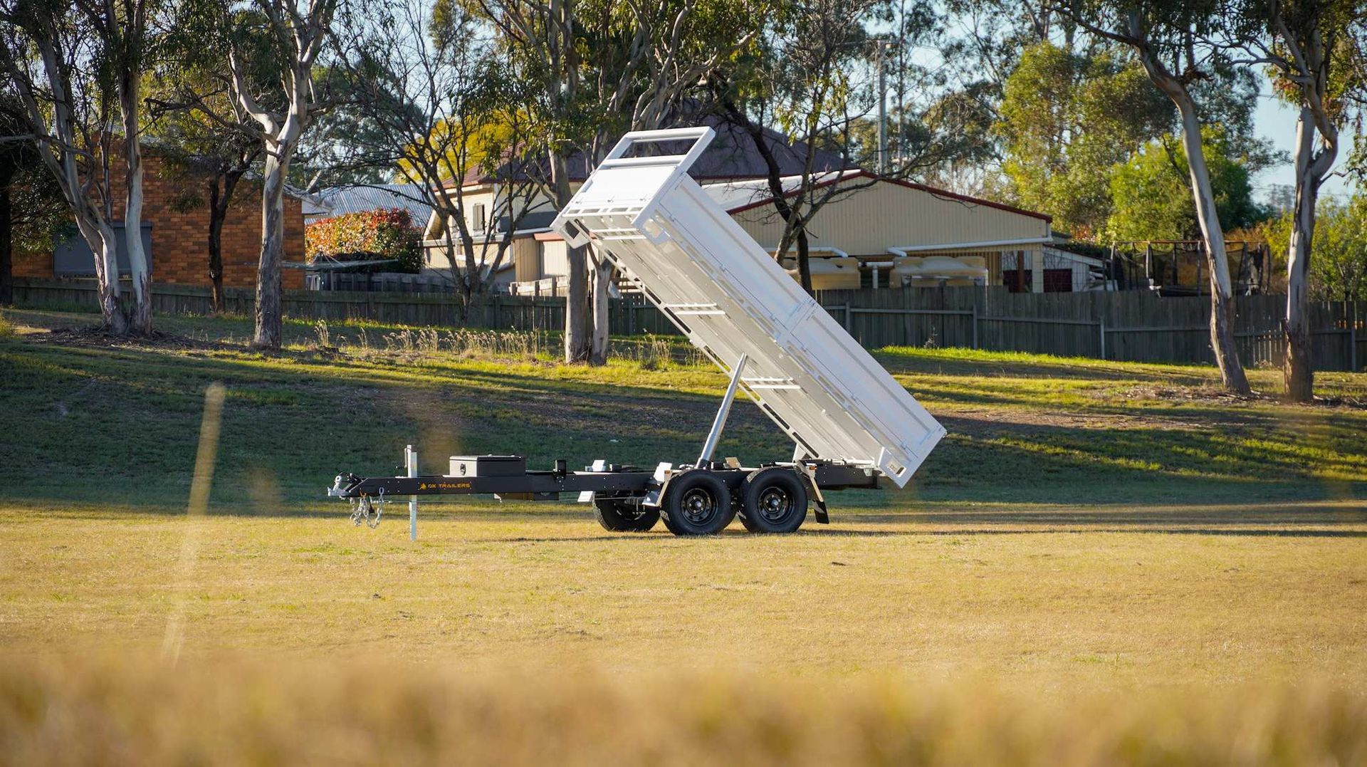 A tipper trailer unloading gravel at a construction site, with extender dropsides, ladder rack, and Aztec Silver upgrade.