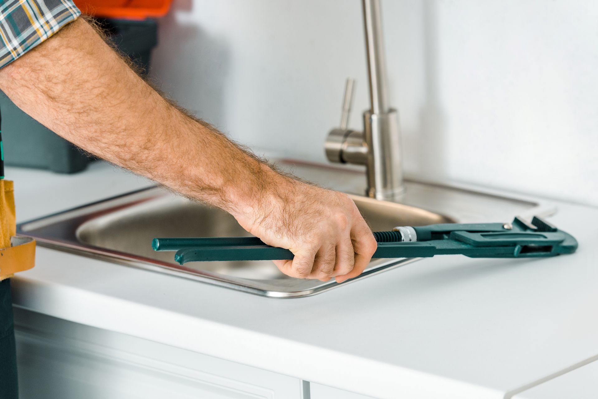 A plumbing contractor is using a monkey wrench to fix a sink in a kitchen.
