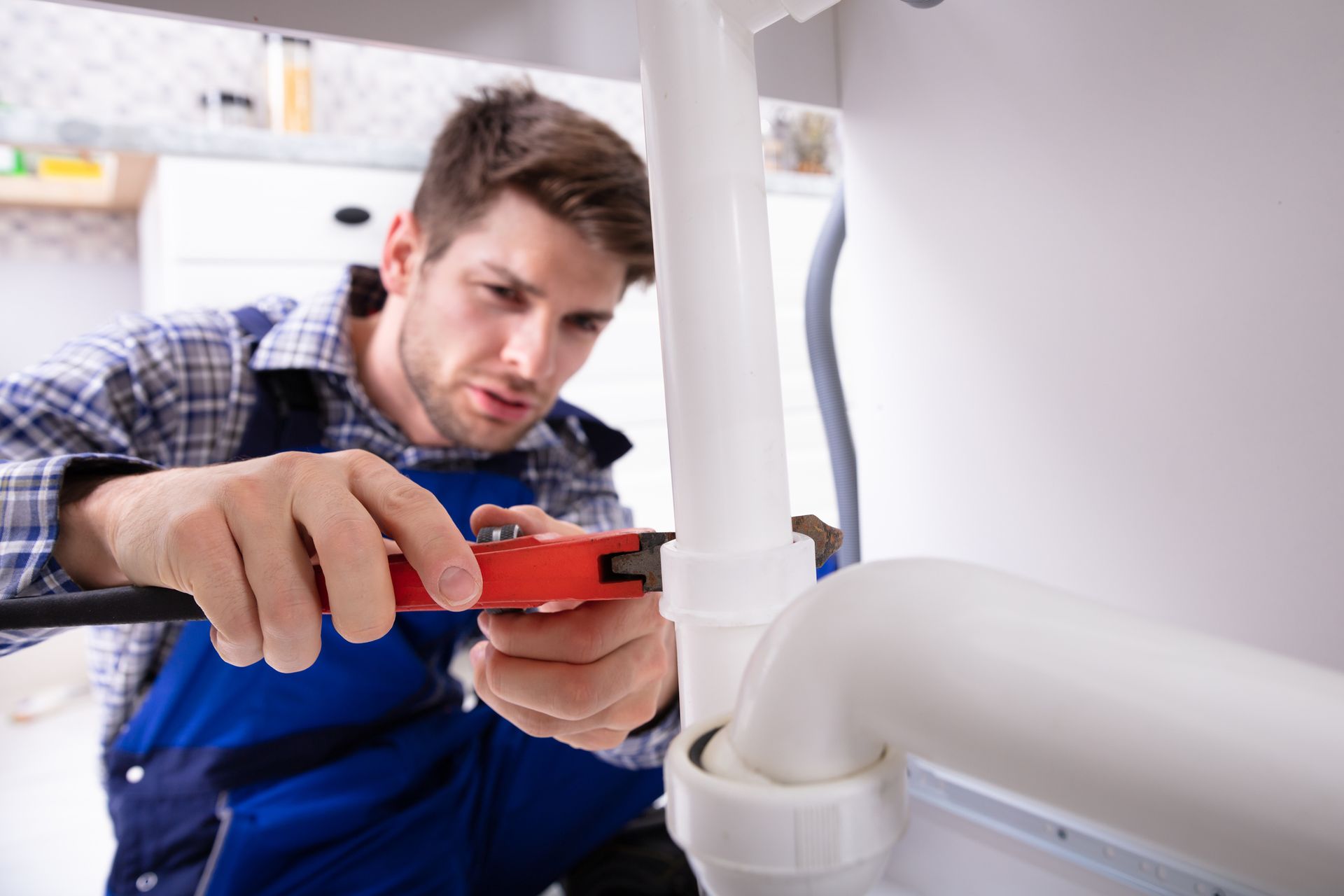 A worker is using a wrench to secure a pipe beneath the sink. A worker is using a wrench to secure a pipe beneath the sink.