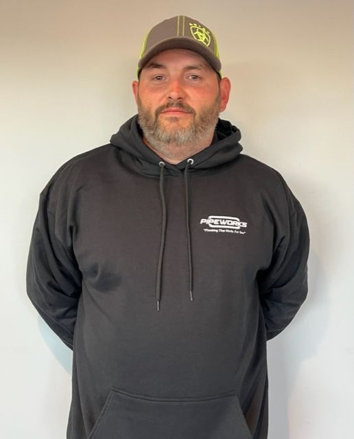 A man wearing a gray and yellow hat and a black hoodie, standing against a plain white wall.