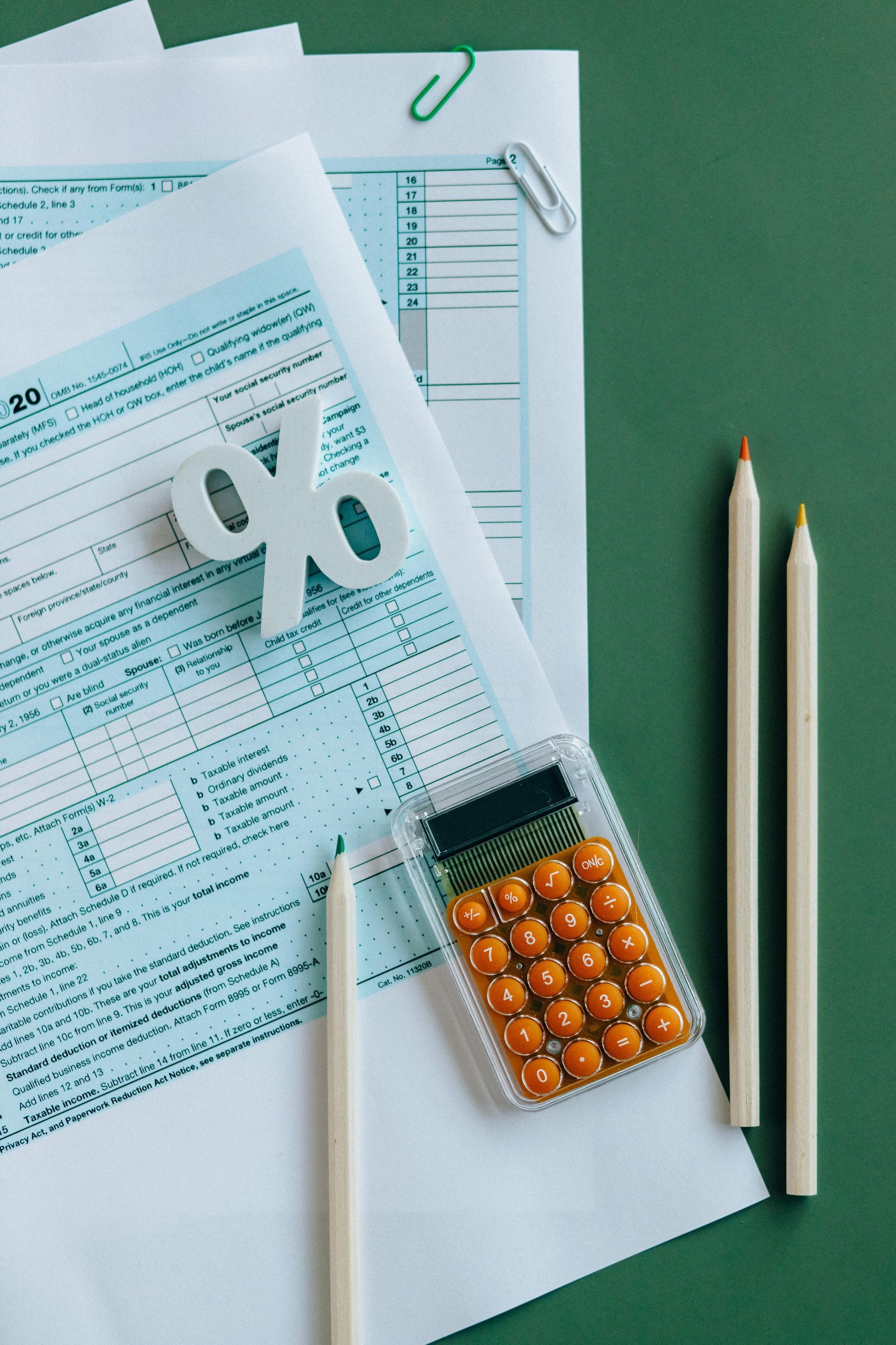 Tax forms and calculator with pencils and a percentage symbol on a green background.