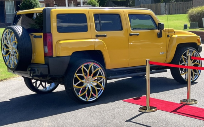 Yellow custom SUV with oversized wheels displayed behind velvet stanchions indoors
