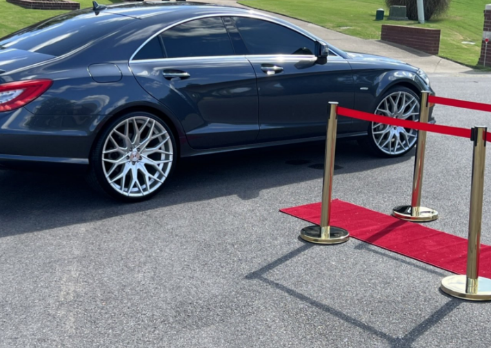 Dark blue sedan on display behind red velvet stanchions outdoors