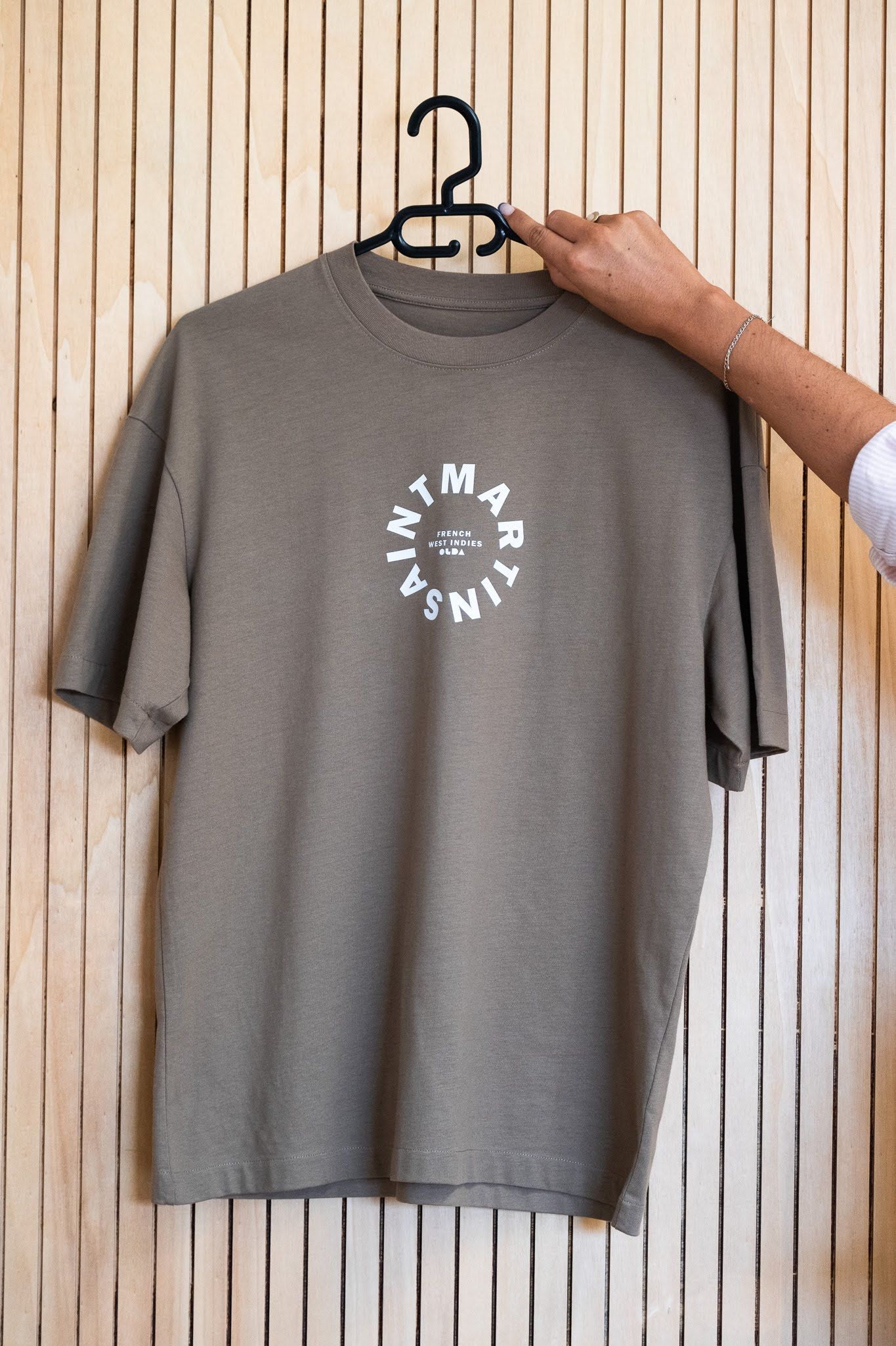 Une personne tient un t-shirt gris accroché à un cintre.