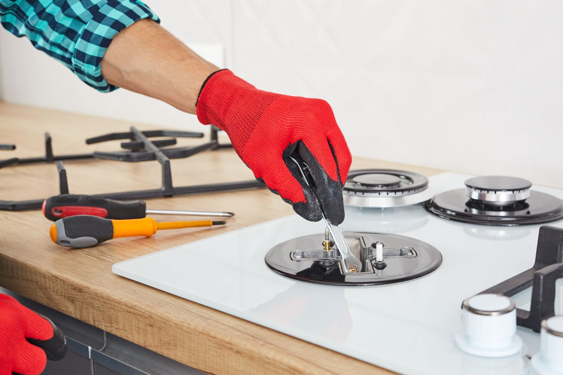 A person is fixing a gas stove with a screwdriver.