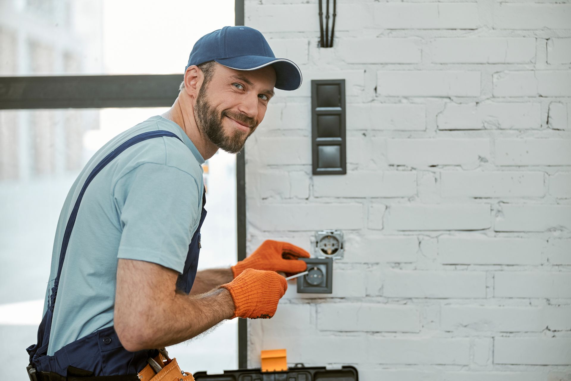 A man is fixing an electrical outlet on a brick wall.