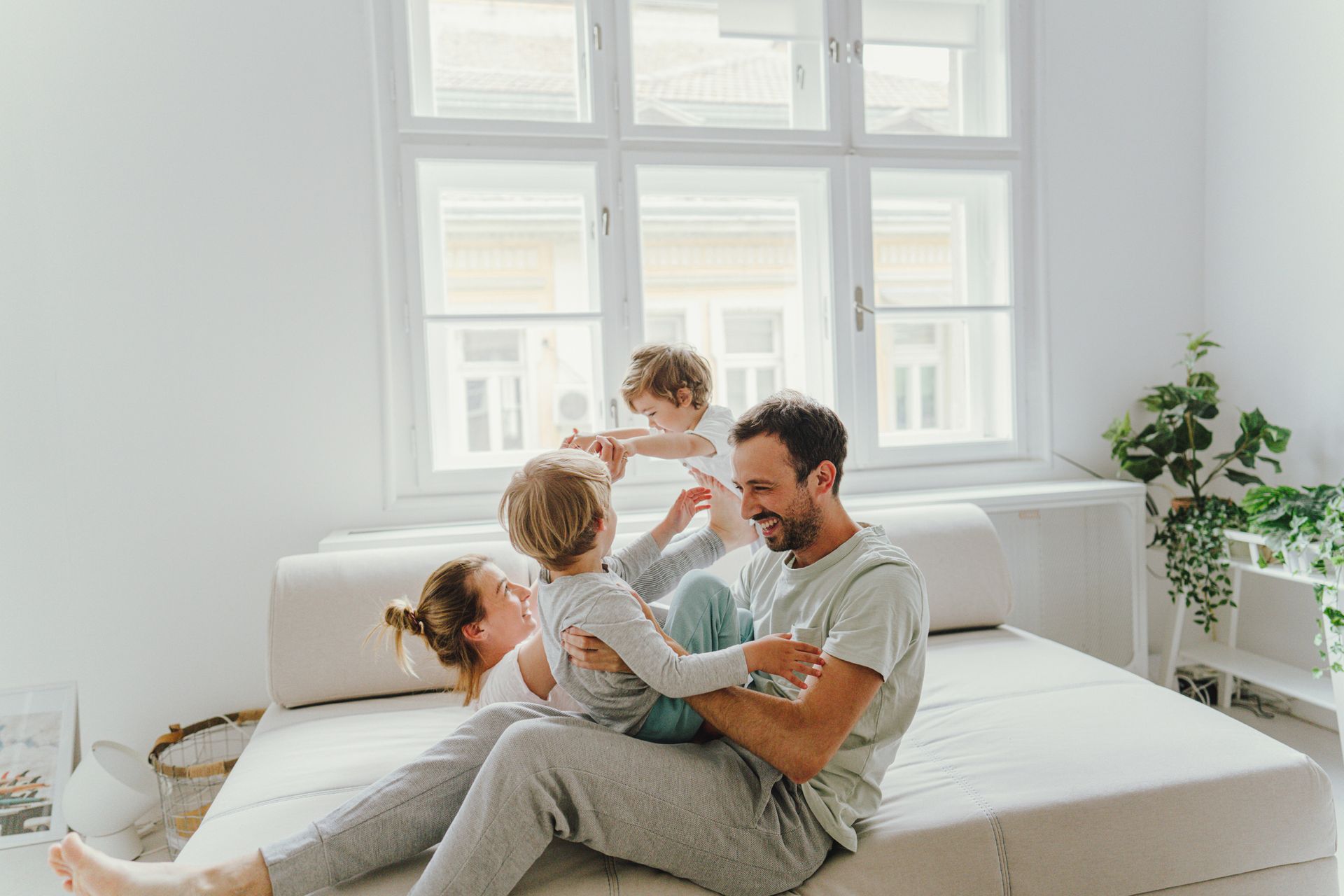 Family of four playing on a bed in a bright room. 