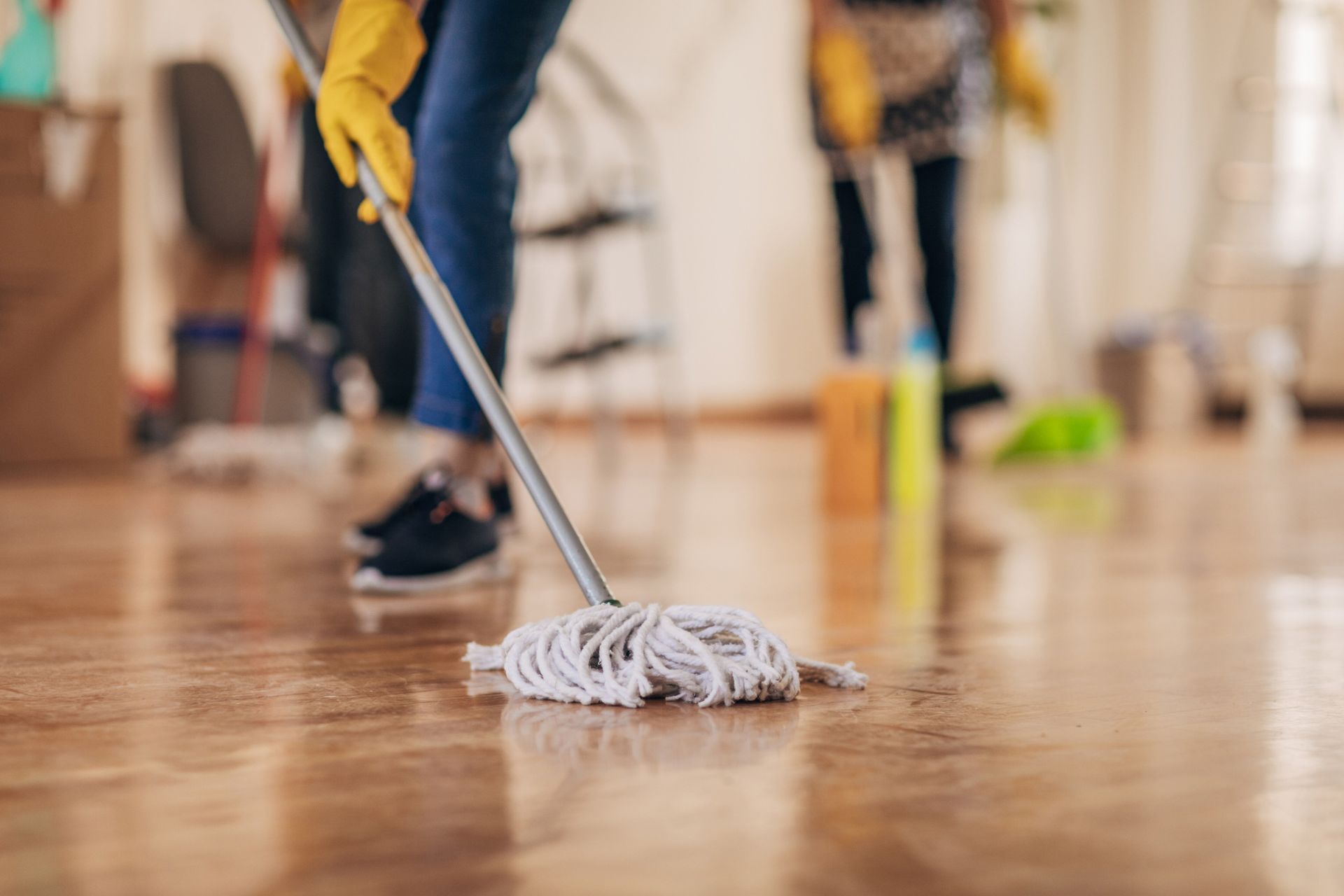 Person mopping a shiny wooden floor, wearing yellow gloves.