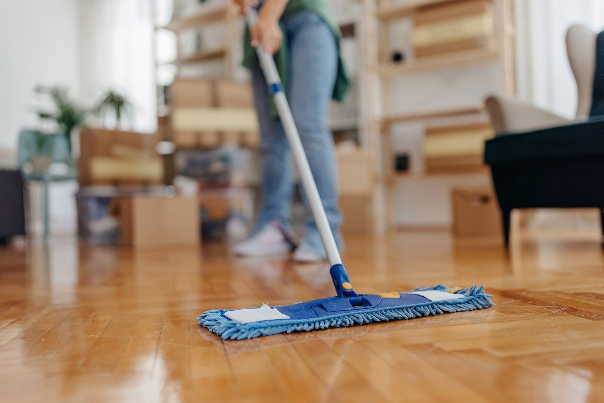Person mopping wooden floor in a well-lit living room, using a blue and white mop.