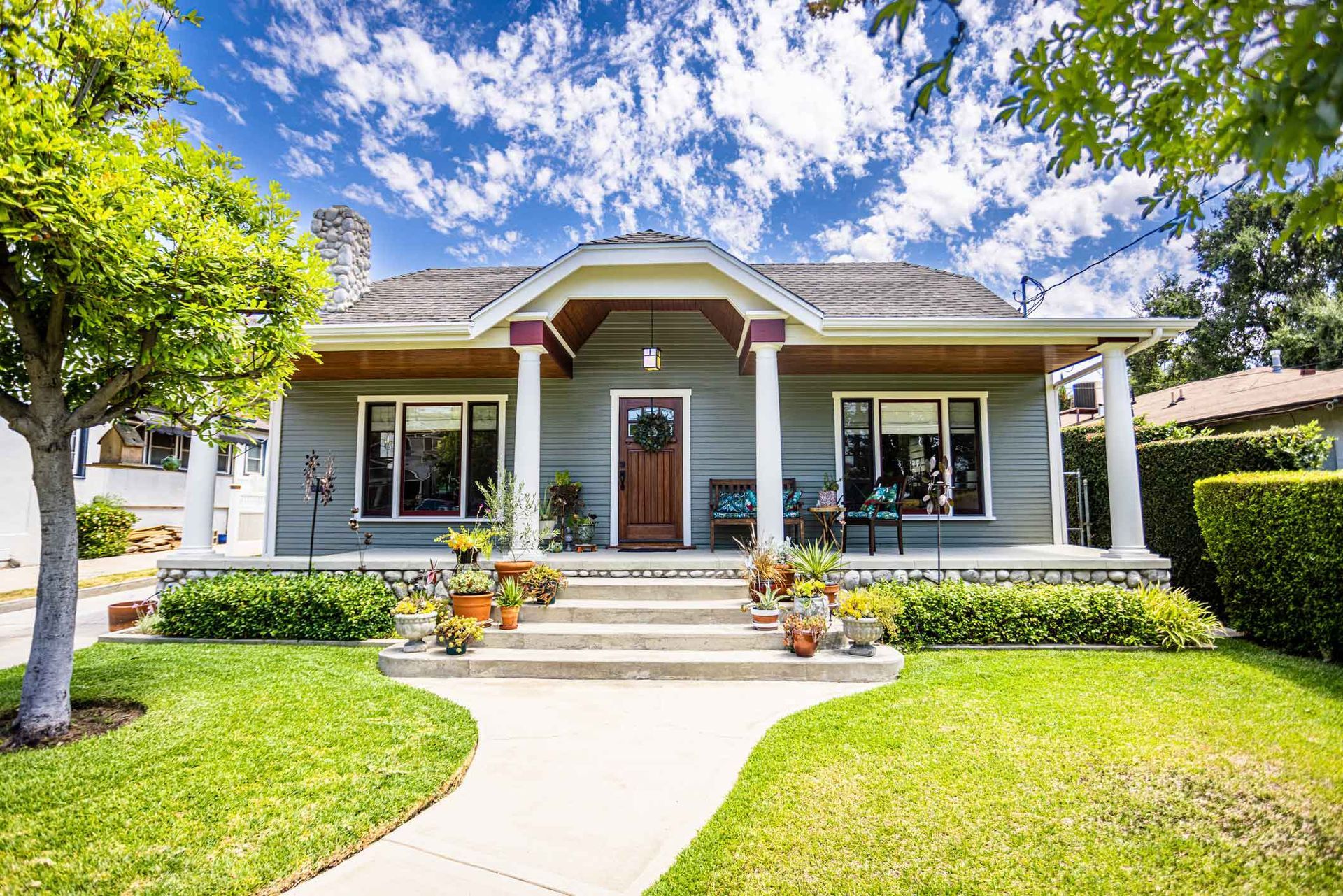 Gray bungalow home with porch, green lawn, and blue sky.
