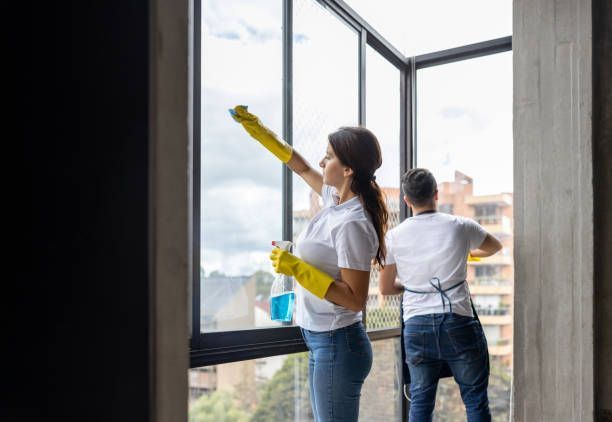 Two people cleaning windows with yellow gloves and spray bottles.