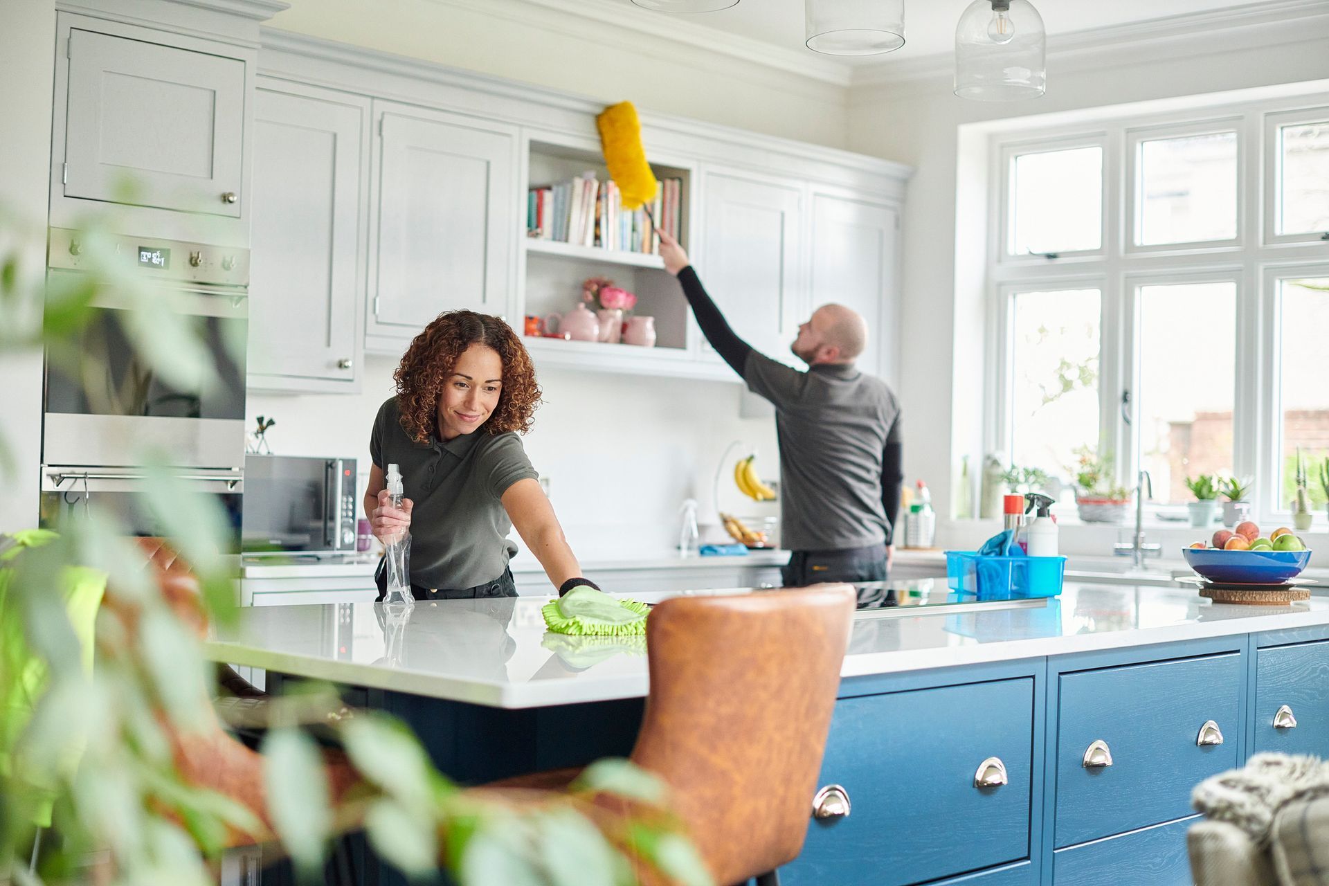 Couple cleaning a kitchen with blue cabinets and white countertops.