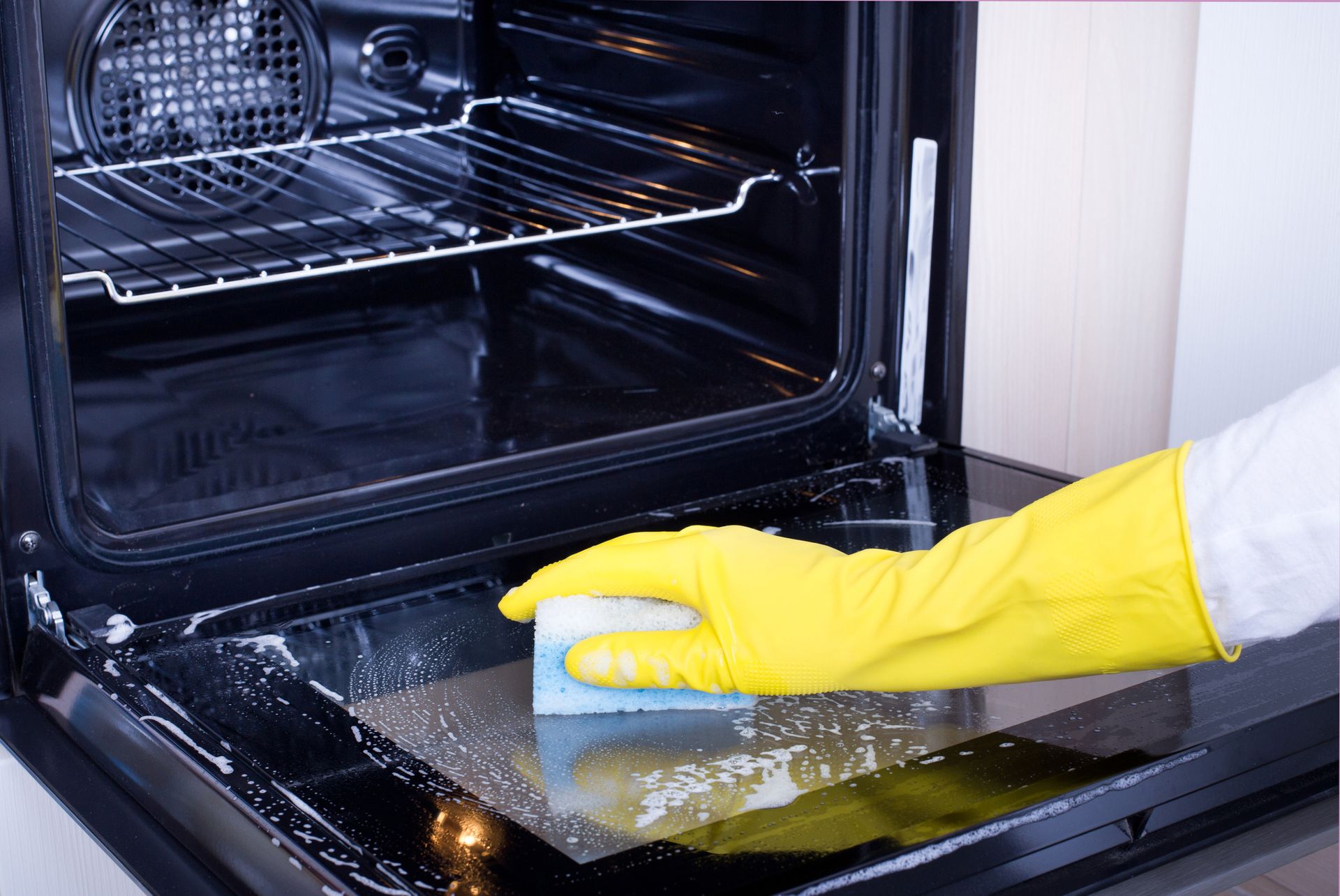 Person wearing yellow glove cleaning oven with sponge.