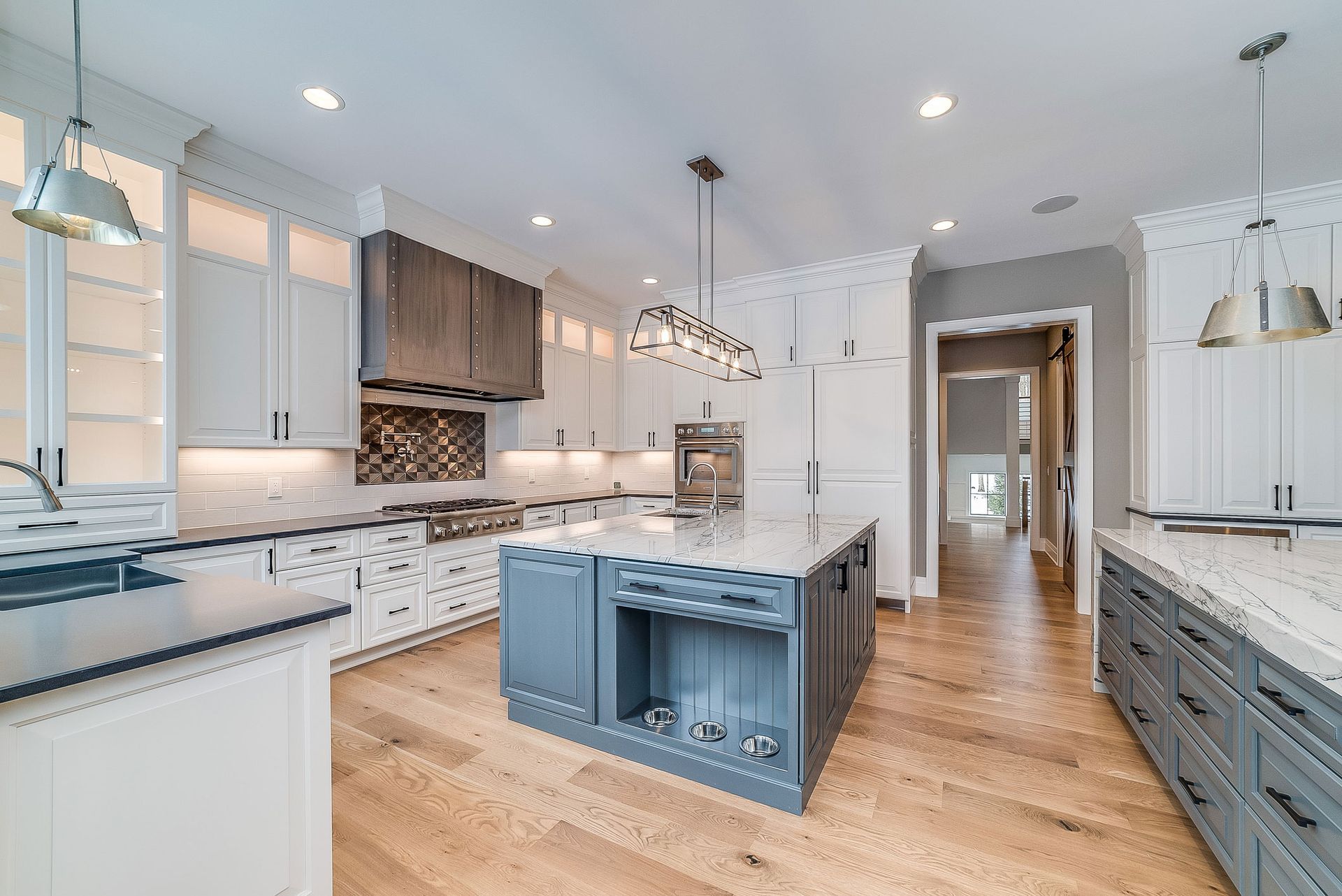 Elegant white kitchen with gray accents, wooden floors, and a blue island.