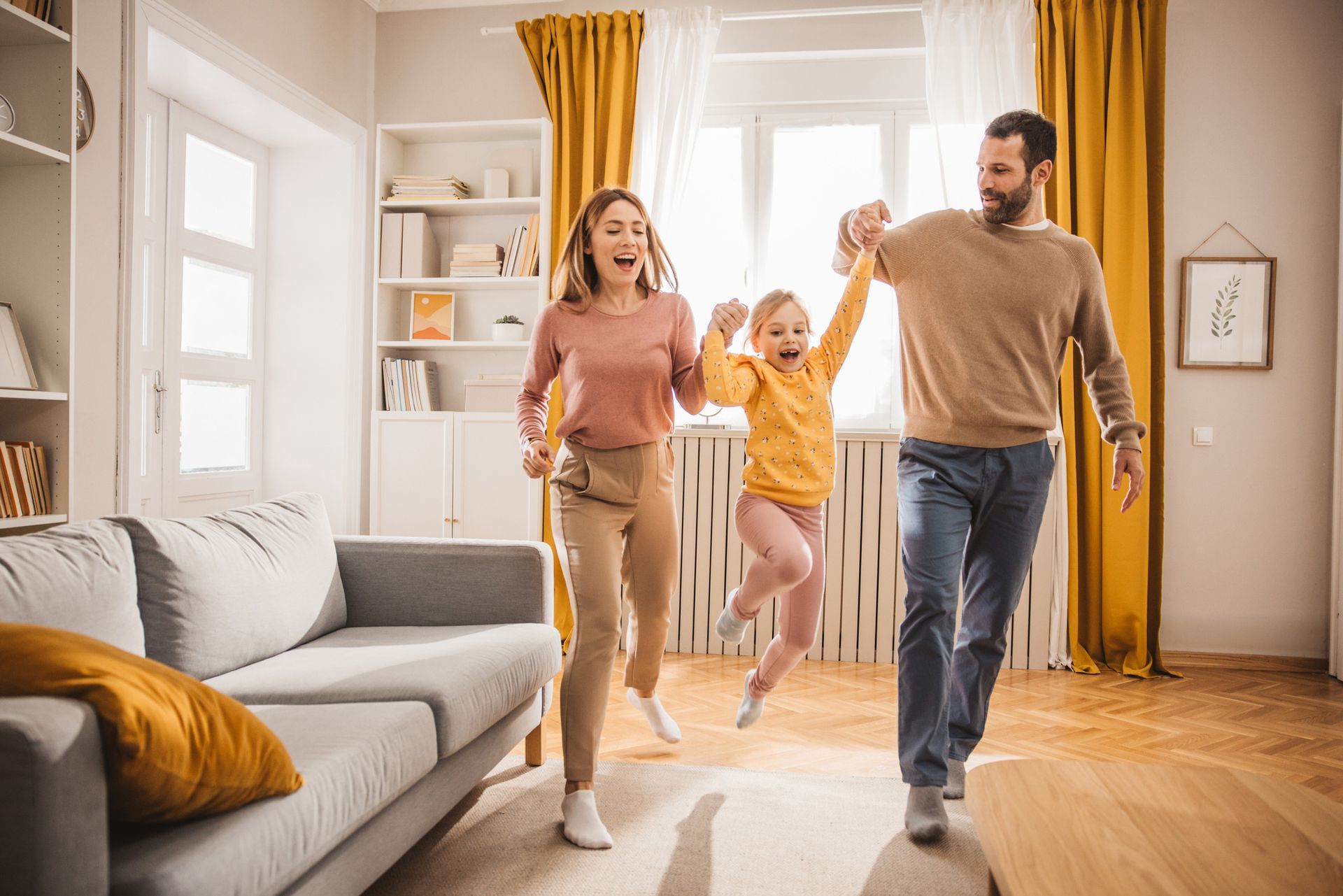 Family, mom, dad, daughter joyfully run and play in a sunlit living room.