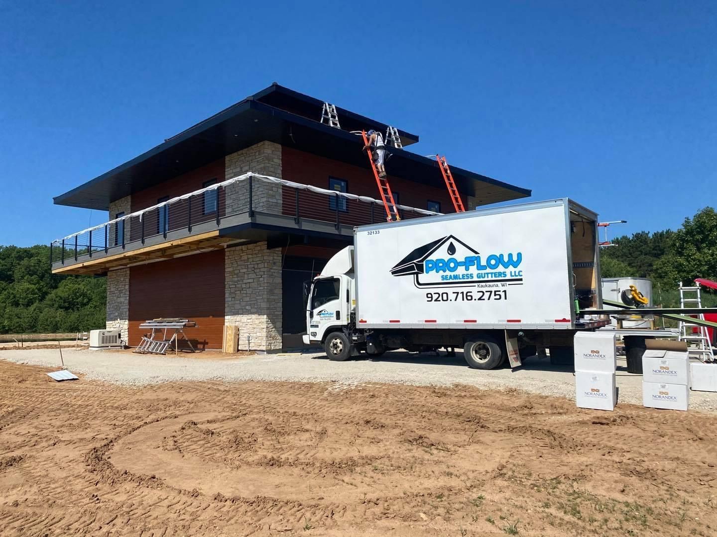 Pro-Flow Rain Gutter truck parked at a construction site while workers use ladders to access the building's roof.