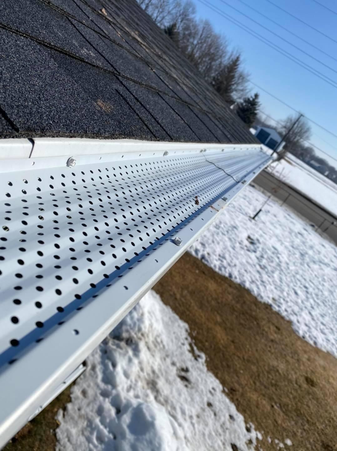 White perforated gutter covers installed on a house roof during a snowy winter day.