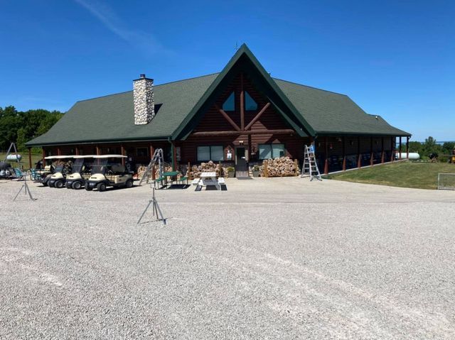 A brown log cabin clubhouse with a dark green roof, stone chimney, and golf carts parked out front on a gravel lot.