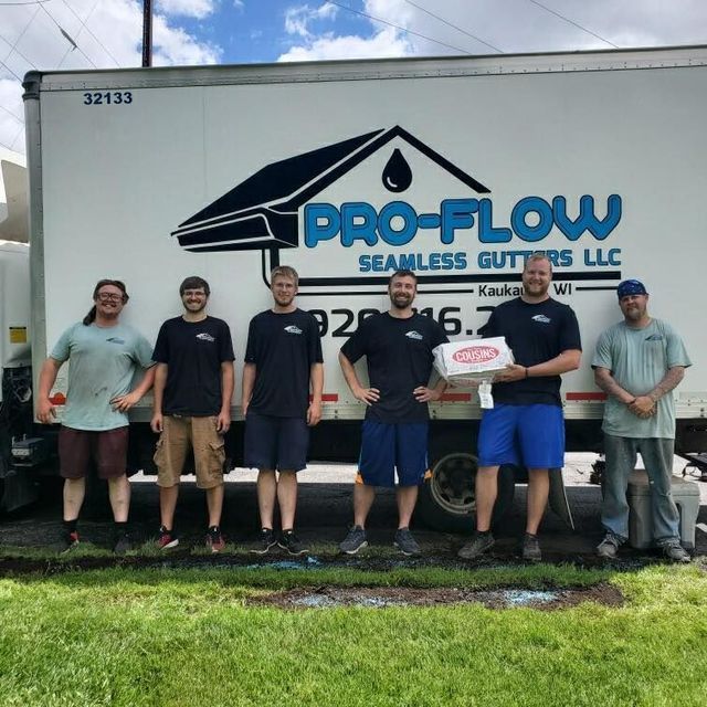 Six people stand in a line in front of a white delivery truck branded with the Pro-Flow Seamless Gutters LLC logo.