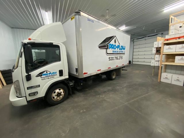 A white Pro-Plow box truck parked inside a bright, spacious warehouse with shelving units in the background.