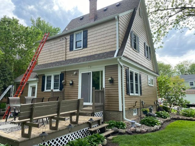 A beige, two-story house with a wooden deck, a wooden bench, and a red extension ladder leaning against the side.