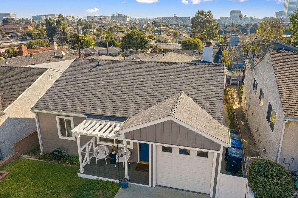 A tan, single-story house with a shingled roof, a front porch pergola, and a one-car garage, viewed from above.
