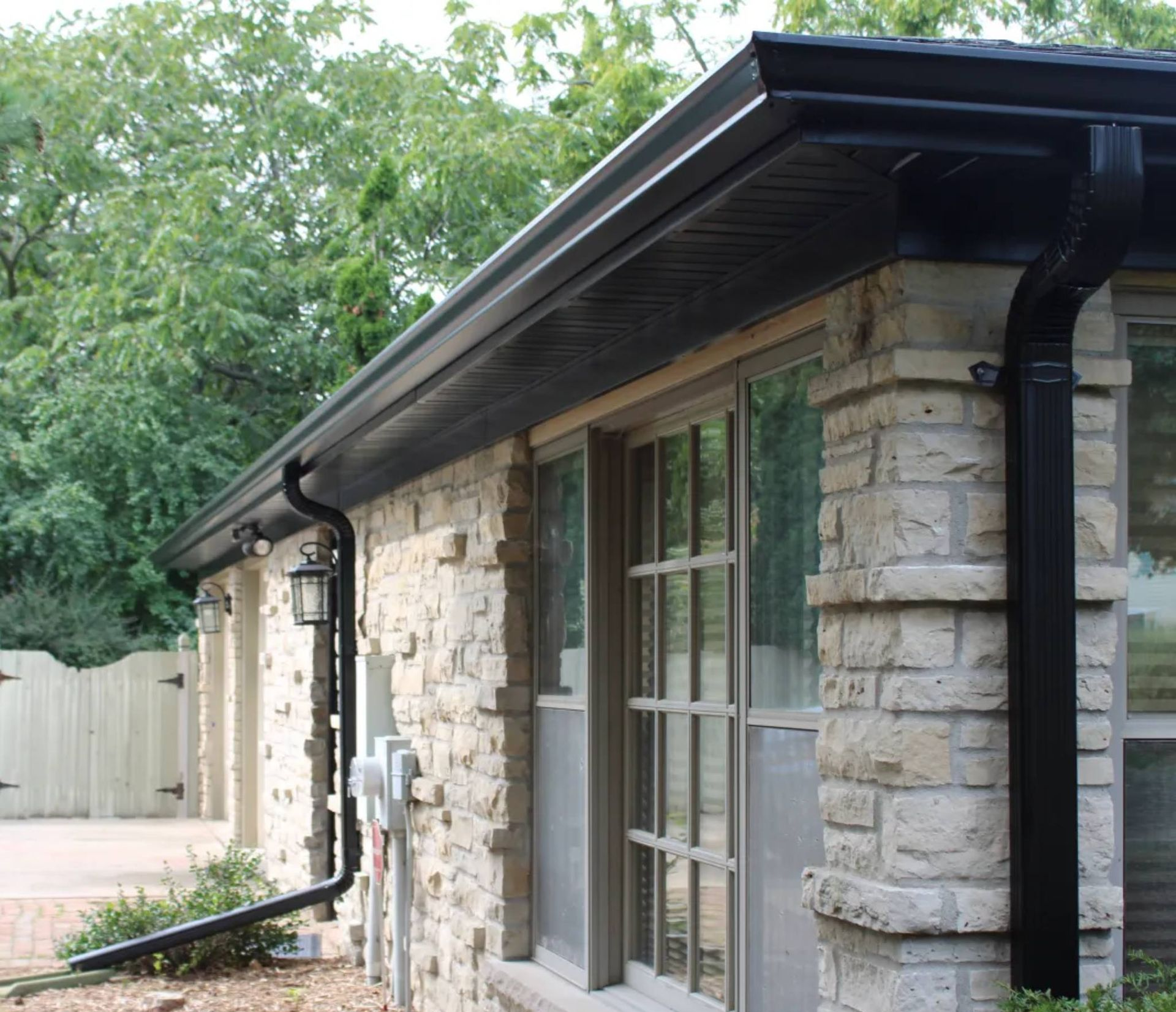 A residential exterior with black gutters and downspouts mounted on a light-colored stone wall.