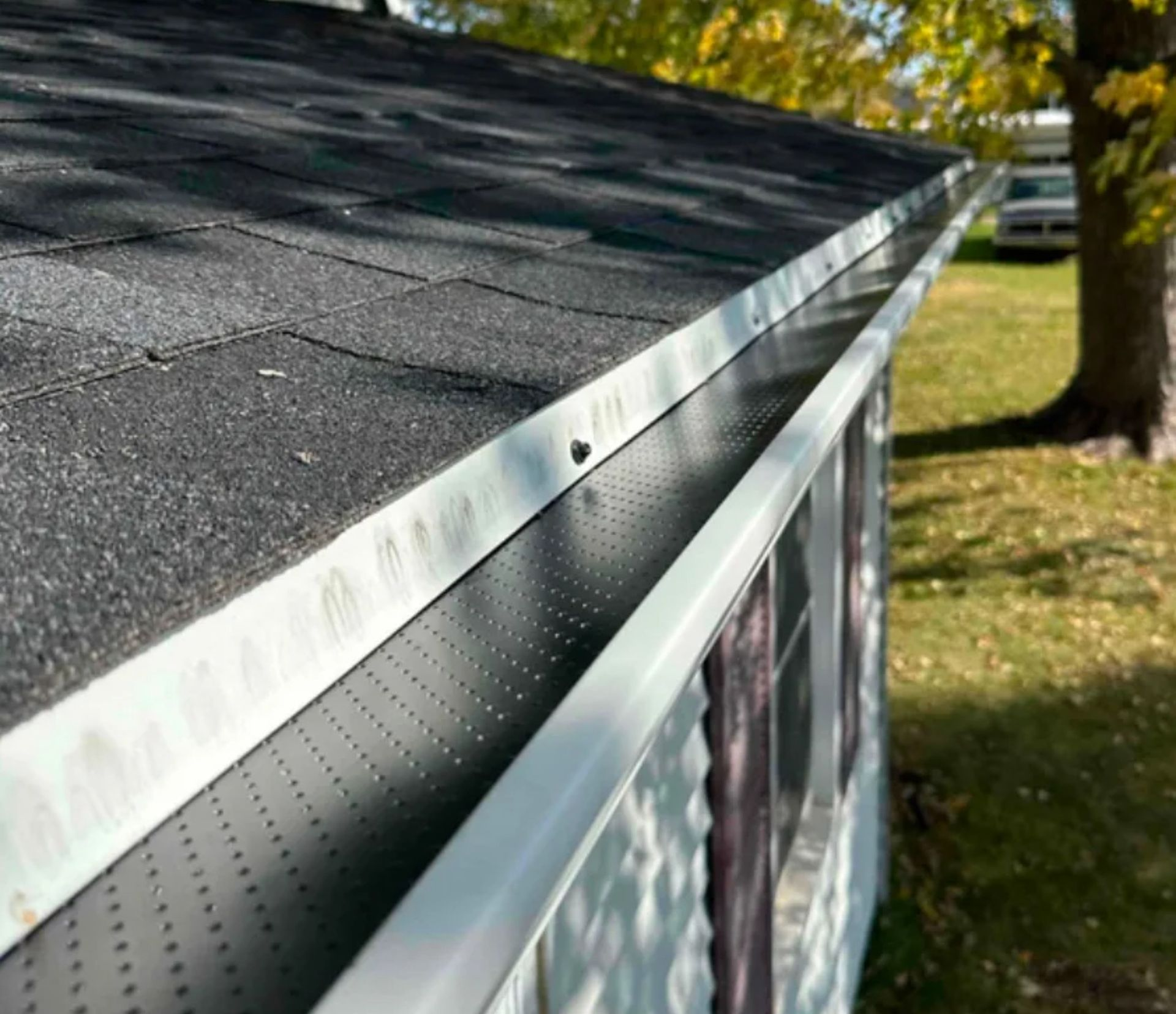 Close-up of a house roofline featuring white gutters with black, perforated metal gutter guards installed.