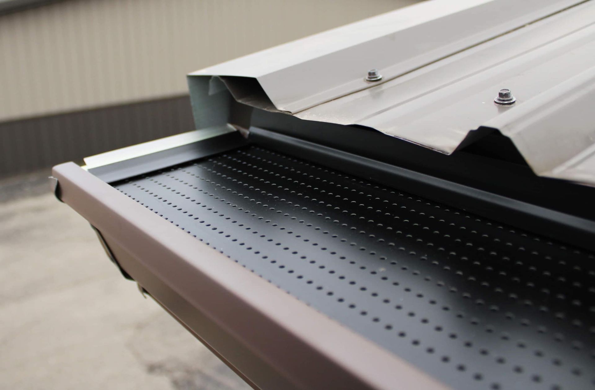 Close-up of a brown gutter with a black, perforated metal gutter guard installed beneath a metal roof.