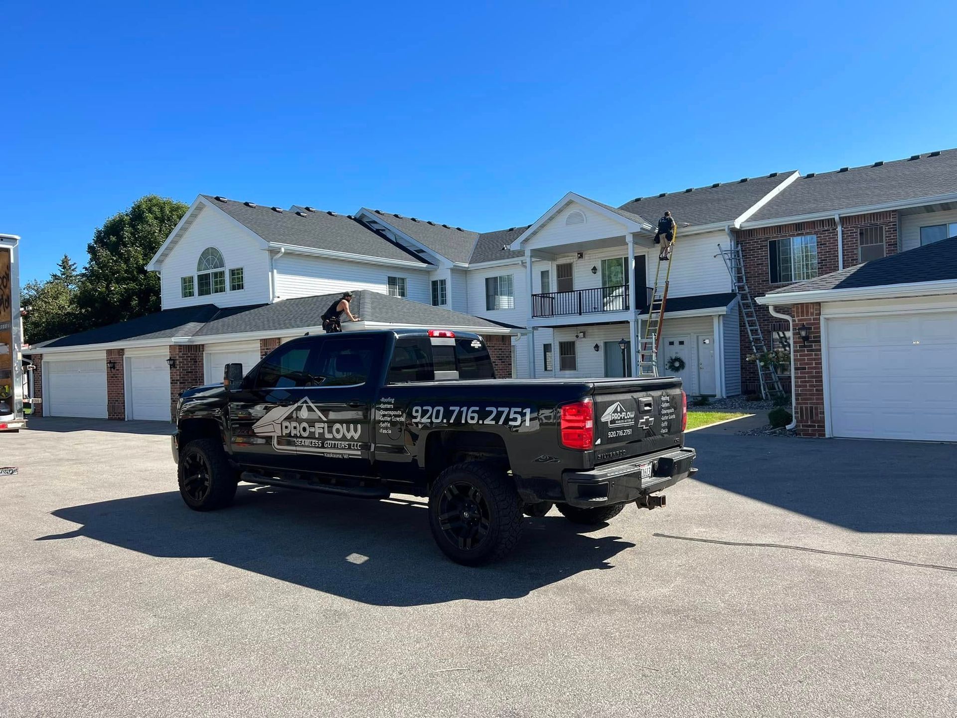 A black pickup truck with business branding parked in front of a white two-story apartment complex on a sunny day.