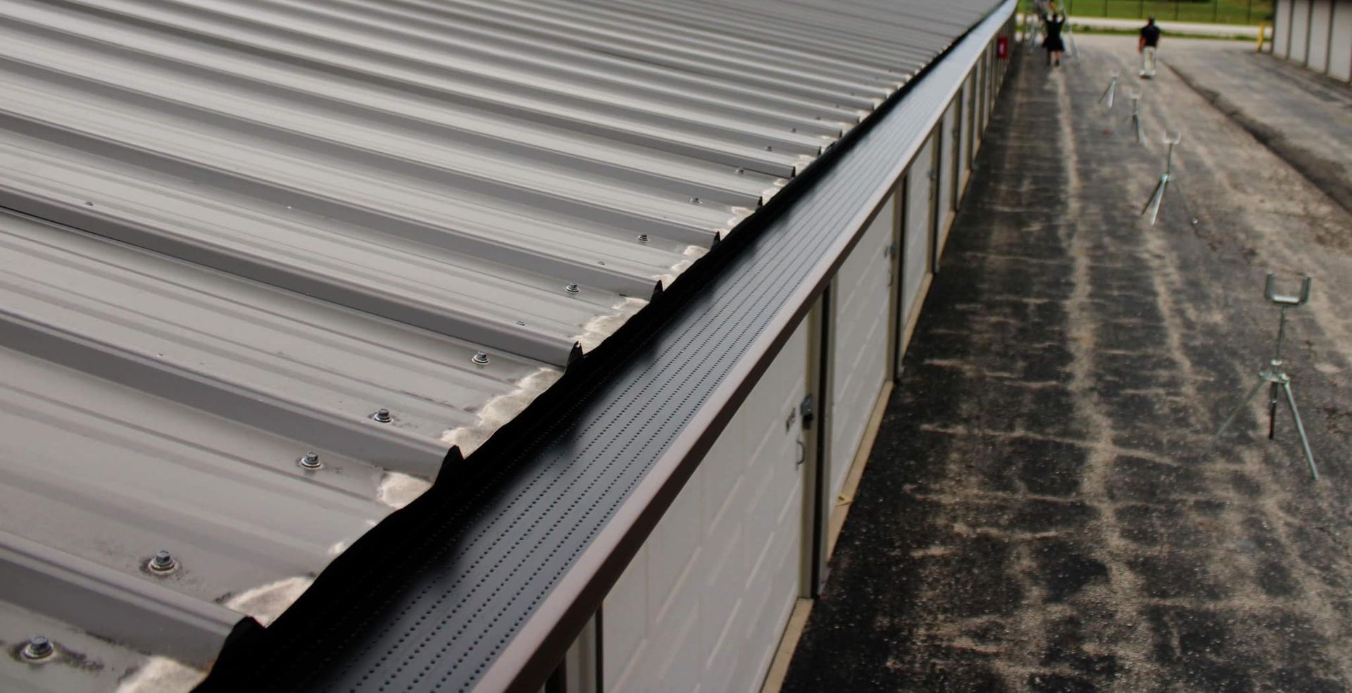 An aerial view of a long metal storage building roof with a dark, perforated gutter guard installed along the edge.