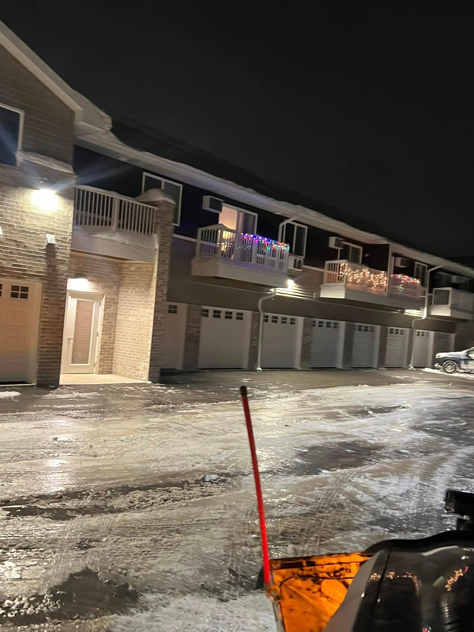 A row of multi-story townhomes with garages at night, with icy, snow-covered pavement in the foreground.