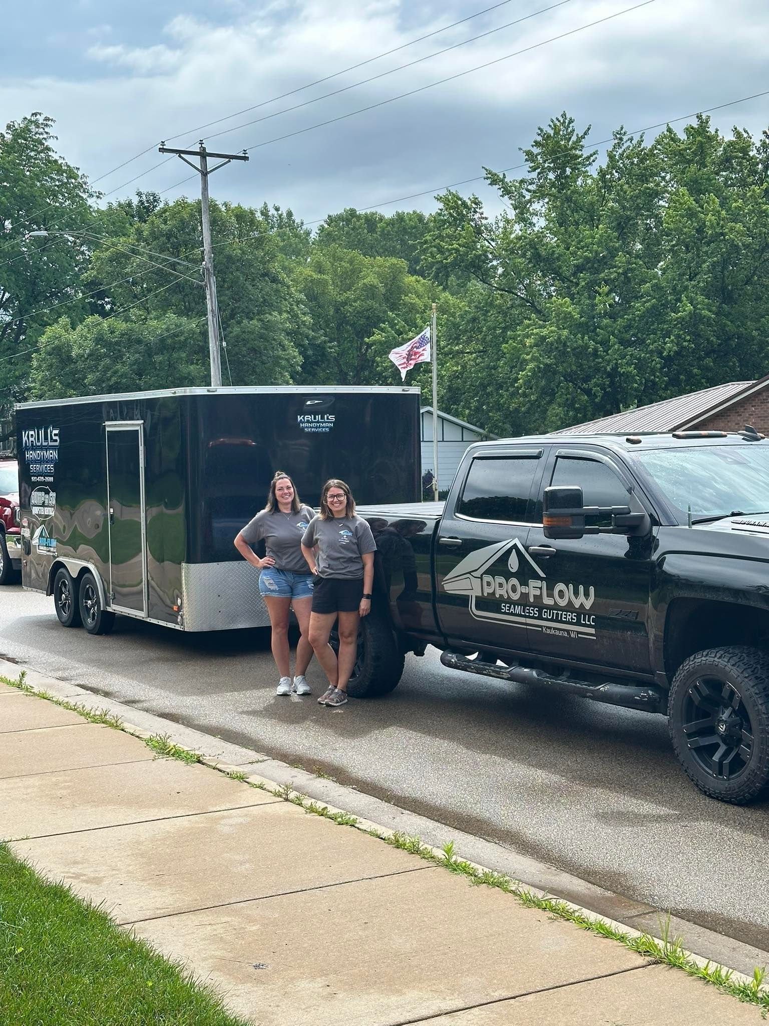 Two people stand next to a black pickup truck with a matching cargo trailer, both labeled with 