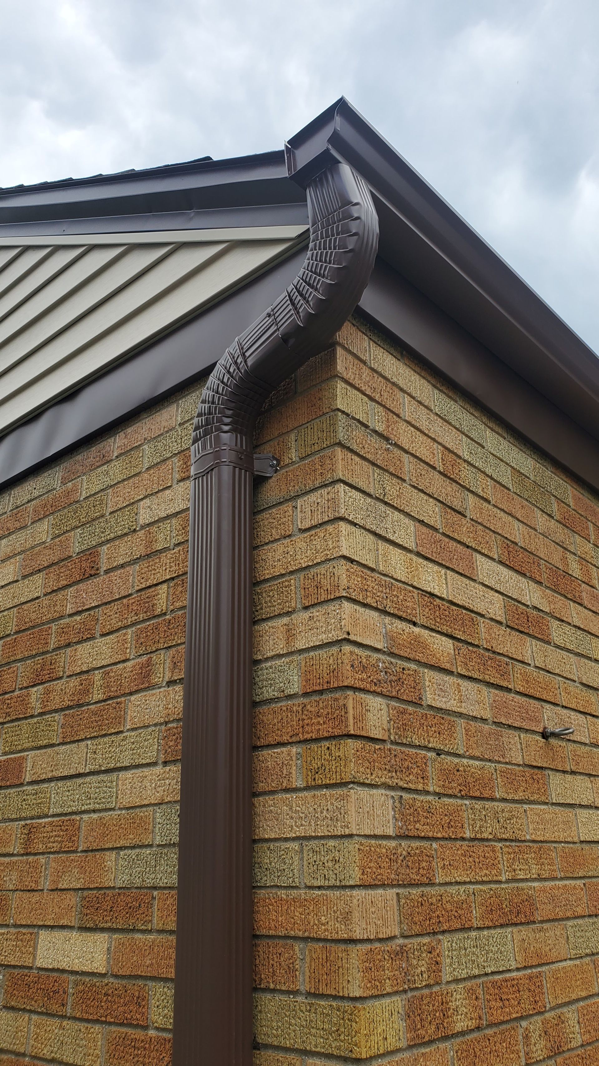 A brown metal downspout connected to the roof gutter of a brick house.
