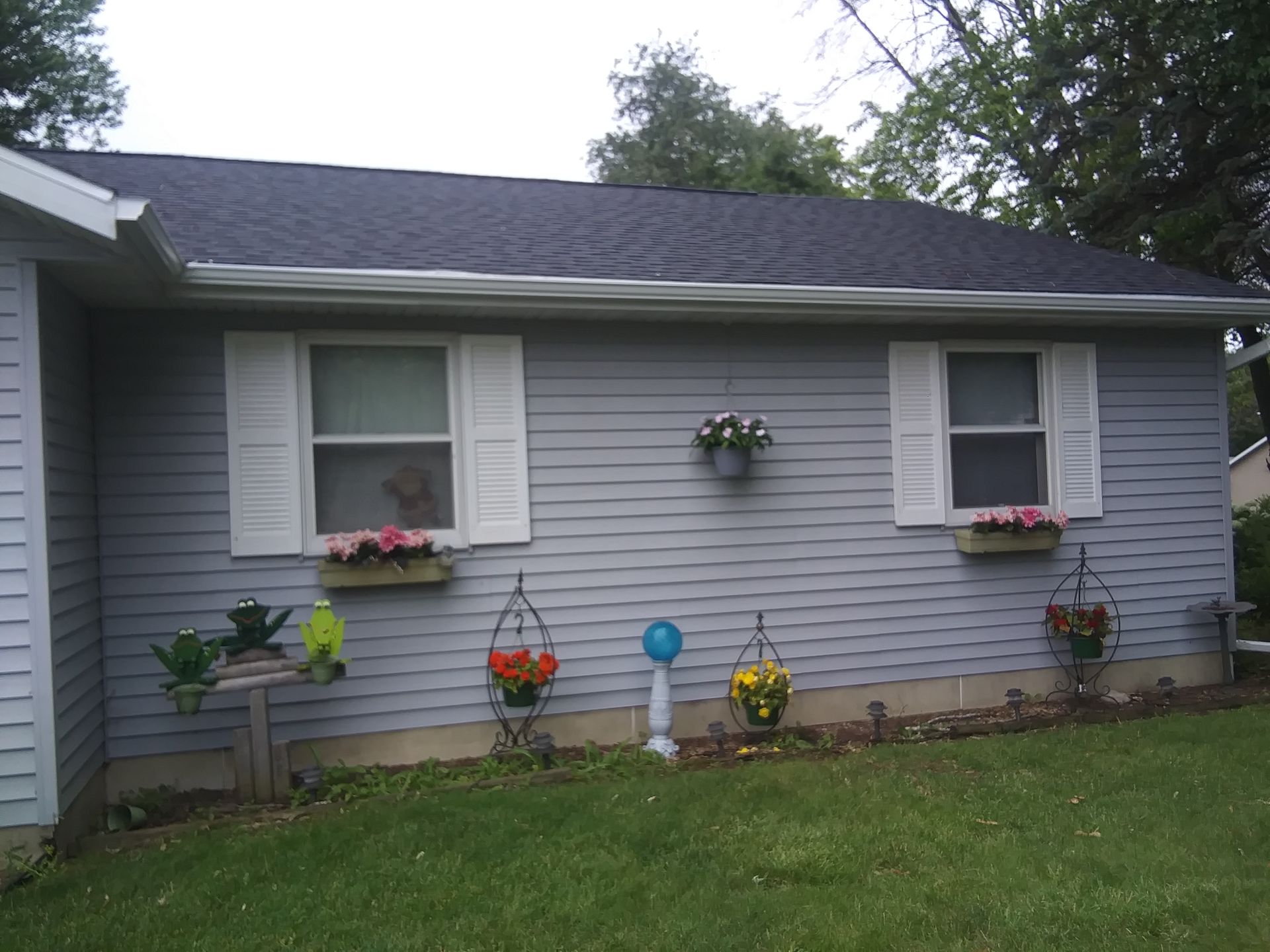 A light blue home exterior with two windows, white shutters, flower boxes, and decorative hanging flower planters.