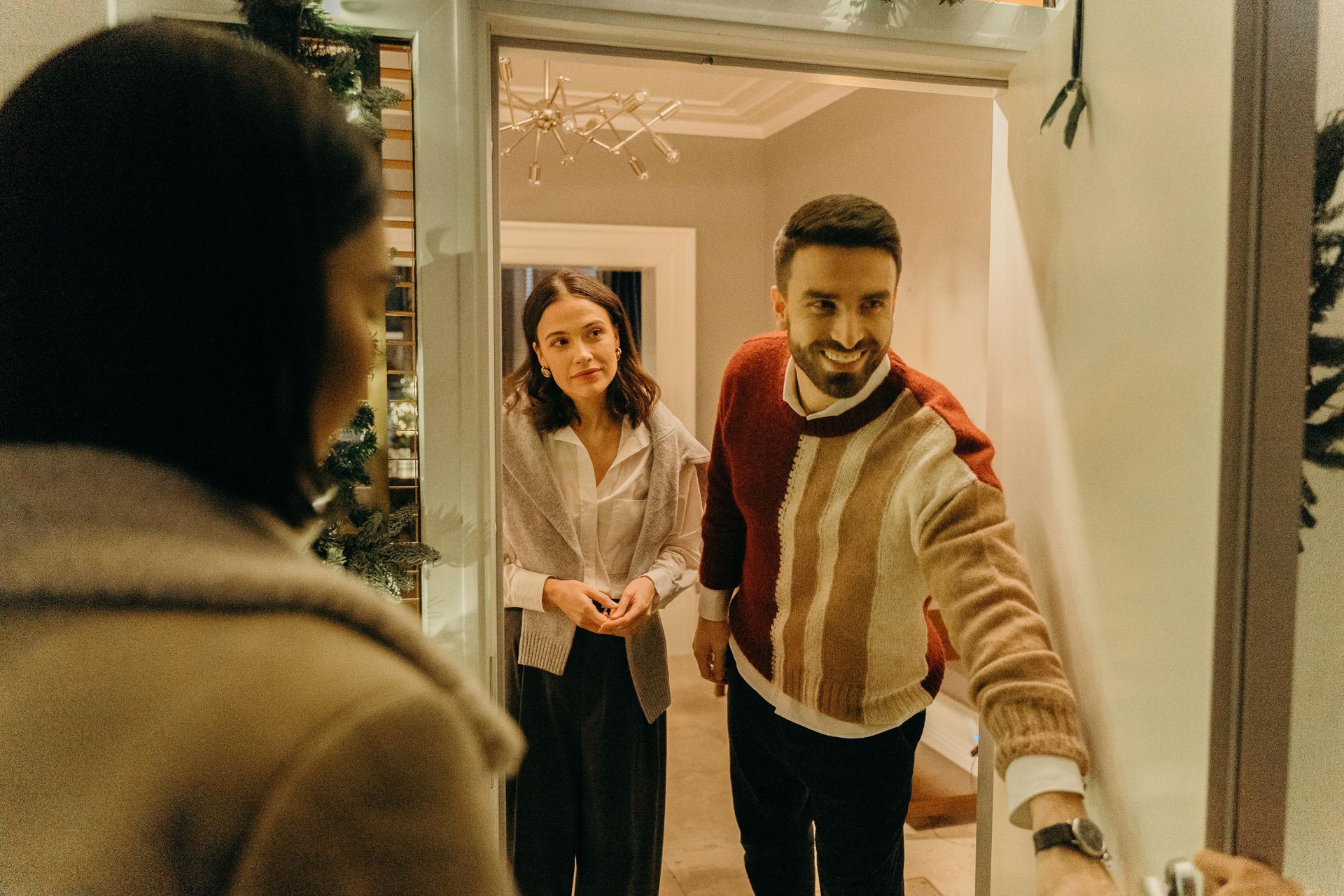 man and woman opening front door to guests at Christmastime.