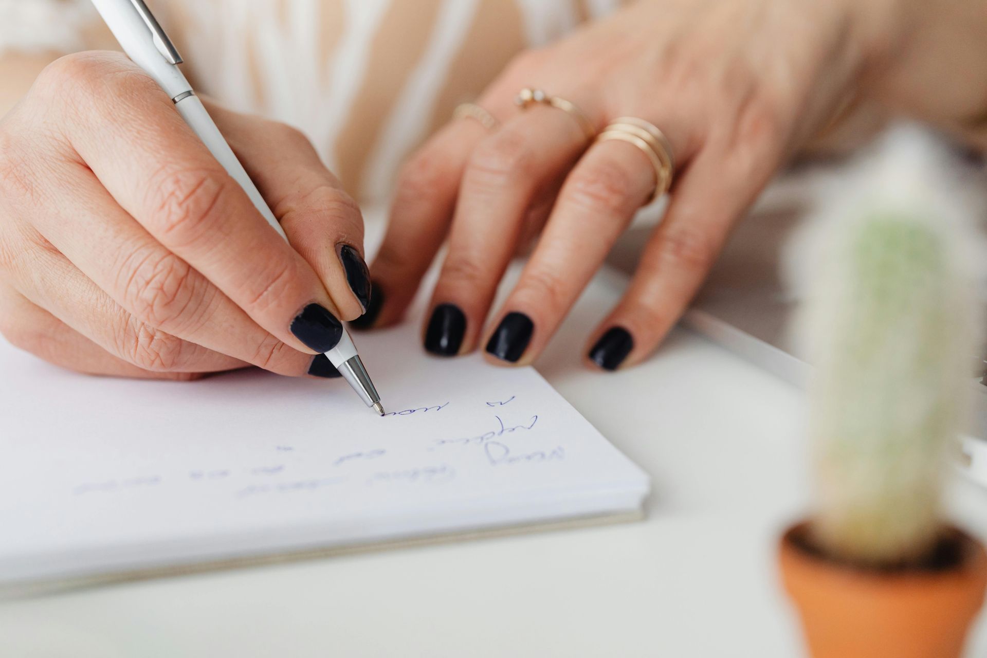 woman writing with a pen in a notebook at a desk. 