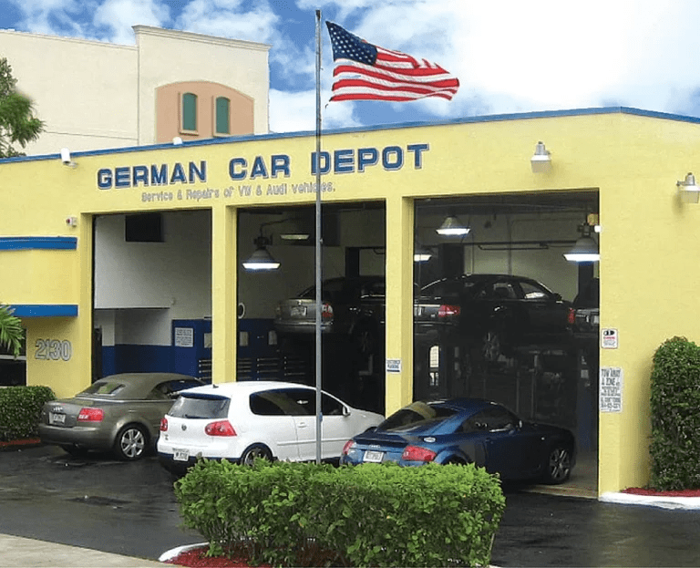 White Audi coupe in an auto repair shop next to blue tool cabinets