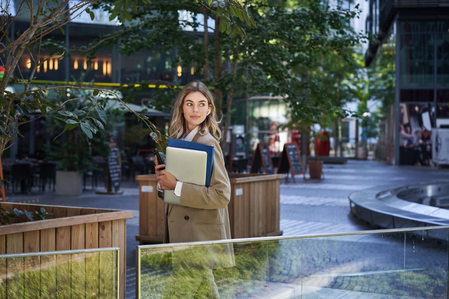 A woman is walking down a street holding a folder and a cell phone.