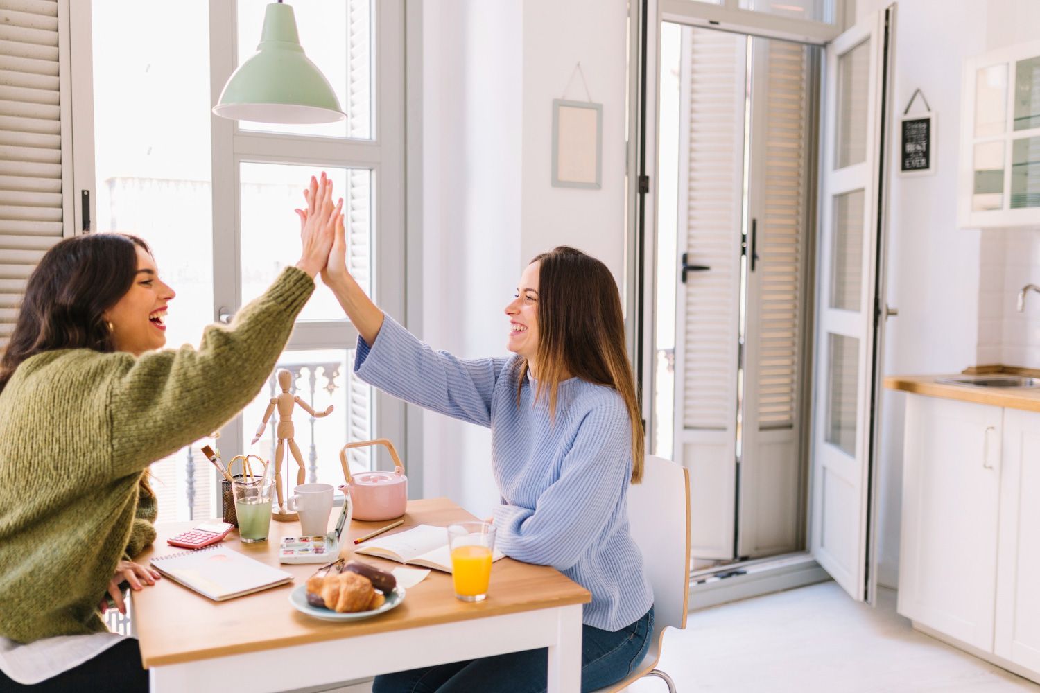 Two women are giving each other a high five while sitting at a table.