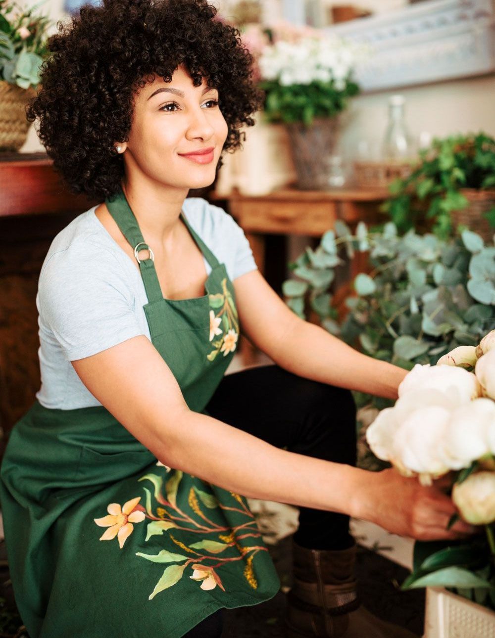 A woman in an apron is kneeling down holding a bouquet of flowers.