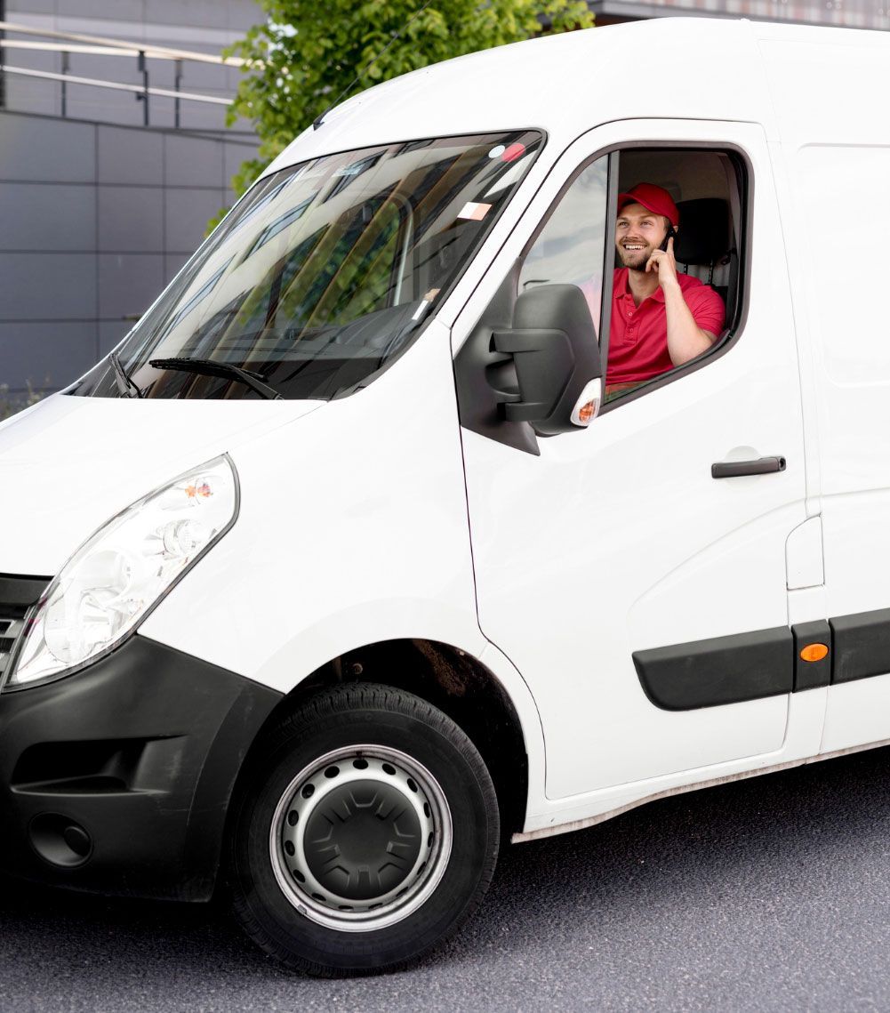 A man is sitting in a white van talking on a cell phone.