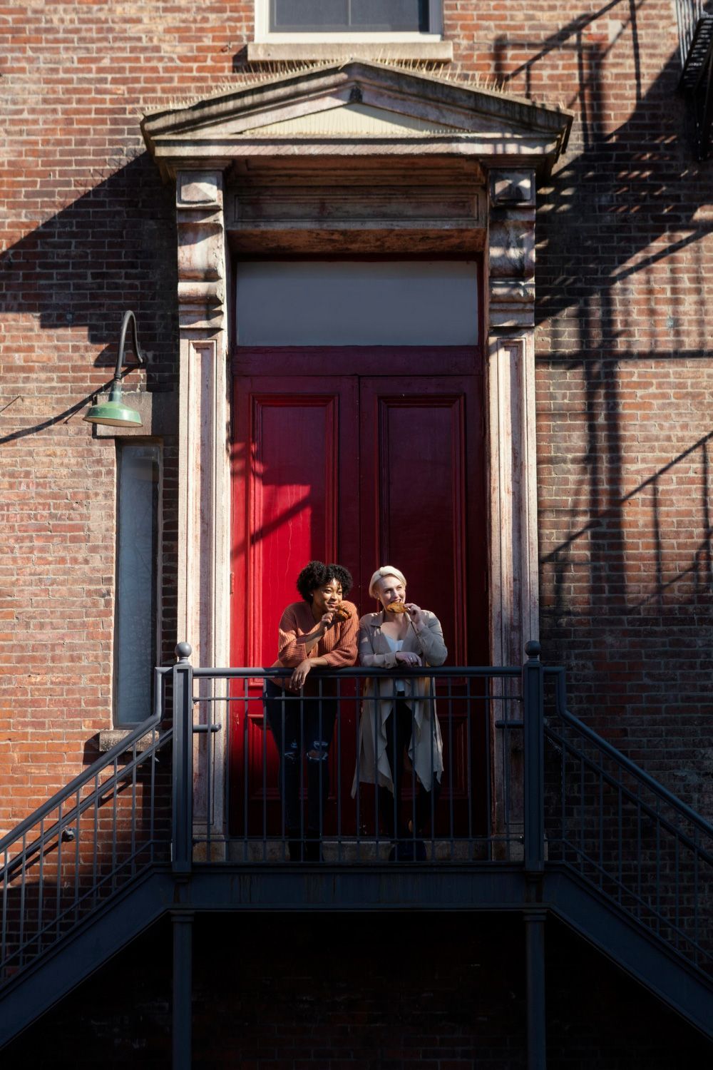 Two people are standing on a balcony in front of a red door.