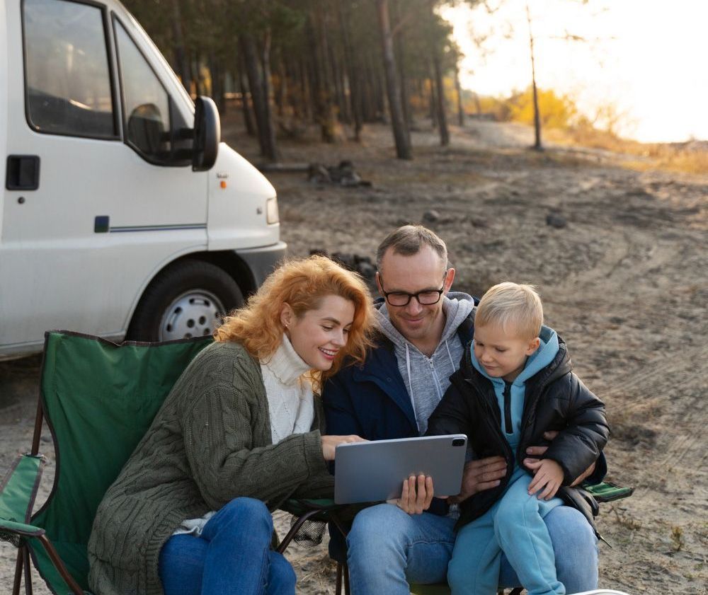 A family is sitting in chairs on the beach looking at a tablet.