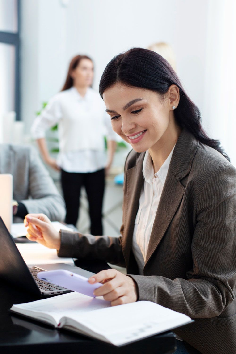 A woman is sitting at a desk with a laptop and a book.