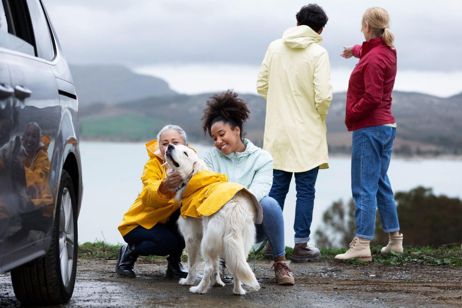 A woman in a yellow raincoat is petting a dog.